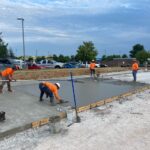 Workers in orange safety shirts smoothing newly poured concrete