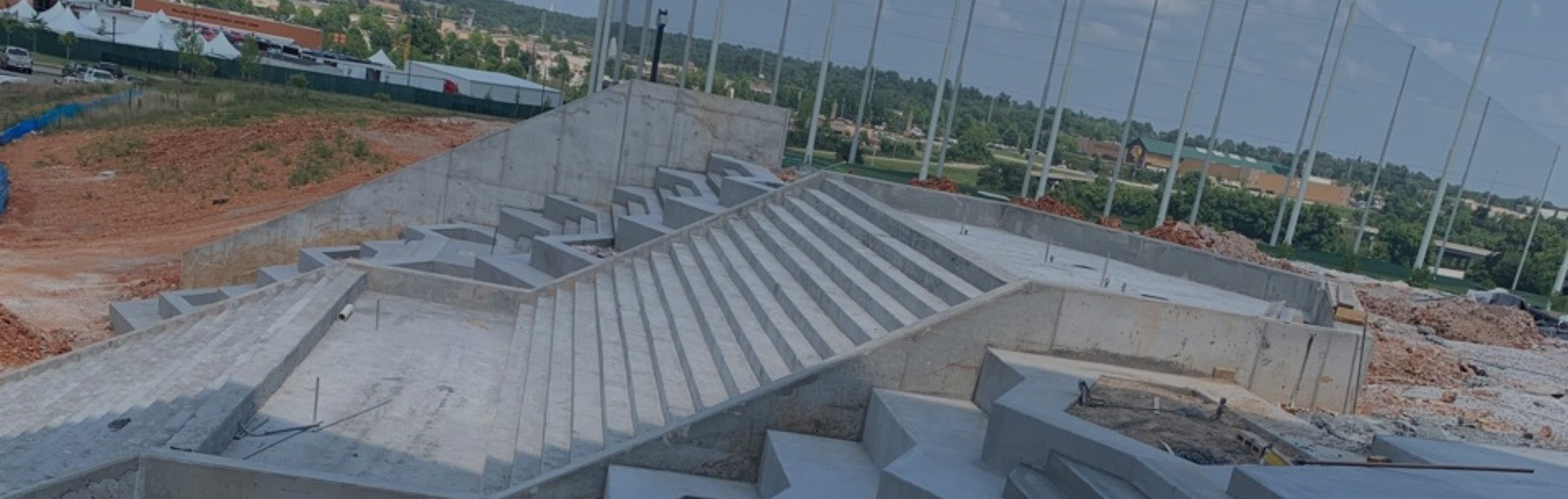 Construction progress of concrete stadium showing installed precast seating tiers, structural supports, and foundation work